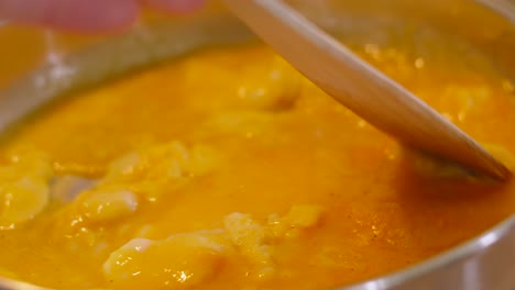 scrambled eggs with butter and milk slowly being stirred in frying pan in kitchen with wooden spatula for protein rich breakfast.