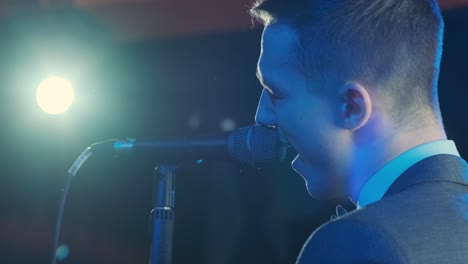 man singing song in microphone during performance on stage on rock concert. close up man rock star singer on music concert on colorful light background