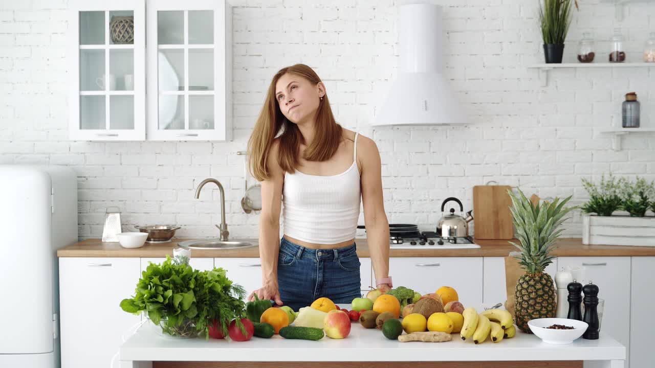 Girl with a tablet chooses recipes. White kitchen and table with vegetables and fruits for a healthy diet