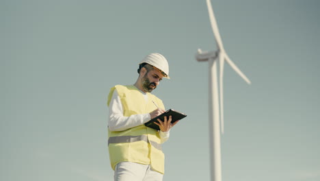 renewable energy engineer uses a tablet to audit wind turbines in a field of clean energy generators on a sunny day, working to save planet earth