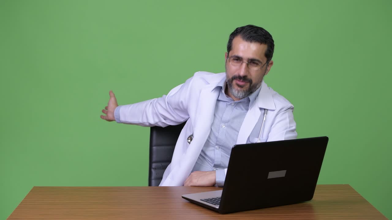Handsome Persian bearded man doctor working with laptop and greeting