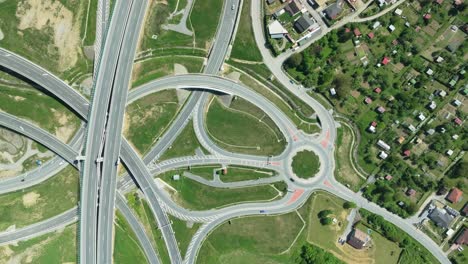 an aerial drone zoom-in shot captures intricate highway junction with cars navigating complex roundabouts and intersecting roads