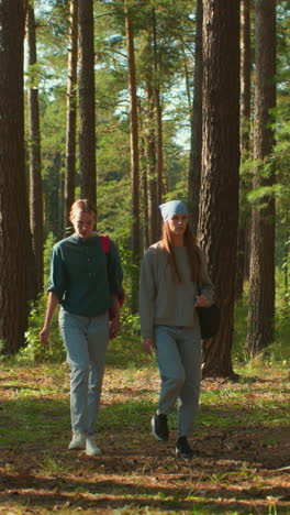 dos hermanas caminando por un bosque iluminado por el sol, una con una mochila y una tela rojas, la otra con un pañuelo azul mirando en la distancia, la luz del sol se filtra a través de los árboles