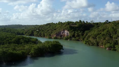 Dolly-out-aerial-drone-shot-of-the-large-winding-tropical-Gramame-river-with-turquoise-water-surrounded-by-foliage-and-cliffs-near-the-tropical-beach-capital-city-of-Joao-Pessoa-in-Paraiba,-Brazil