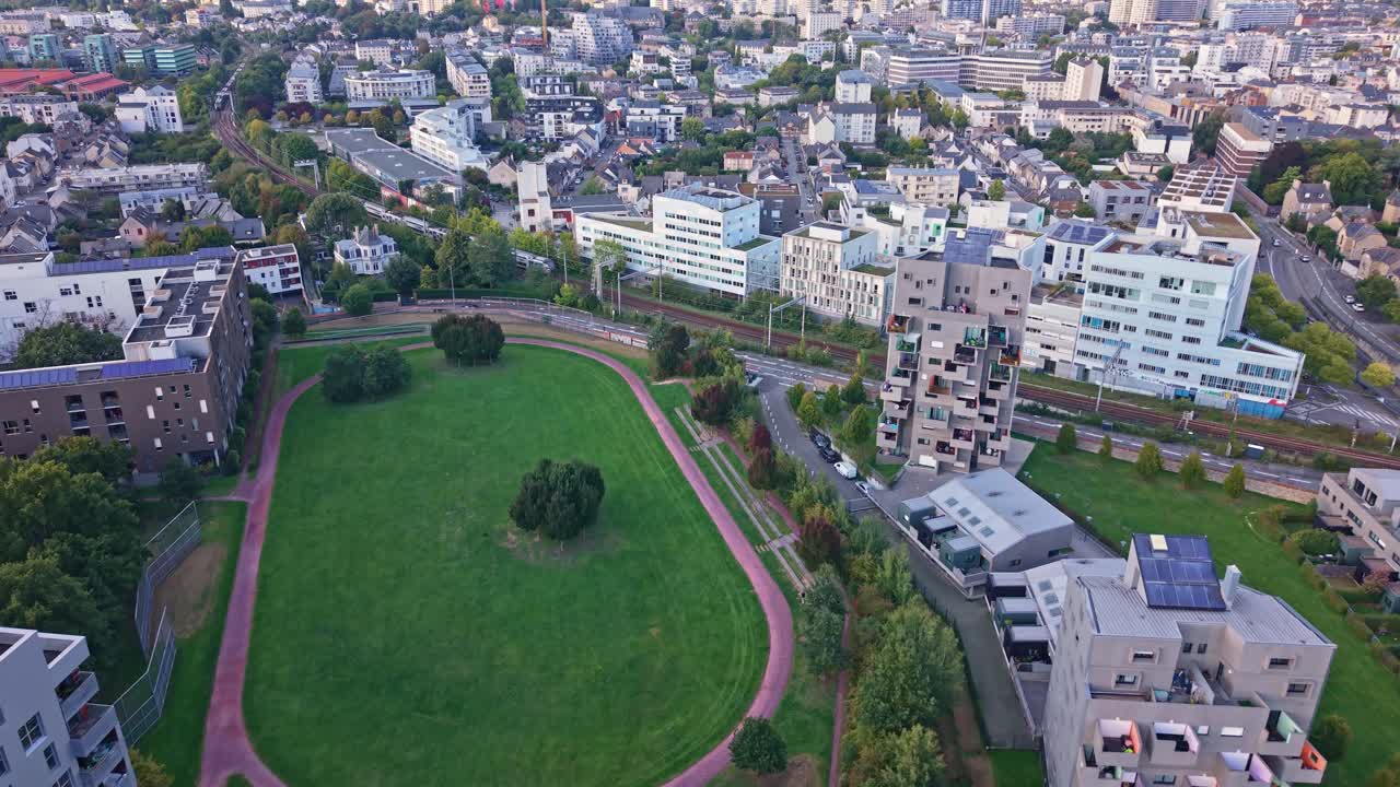 Aerial drone view of the La Courrouze eco-district in Rennes, France. Features modern apartment buildings, a large green park with walking paths, and the railway line in a sustainable neighborhood