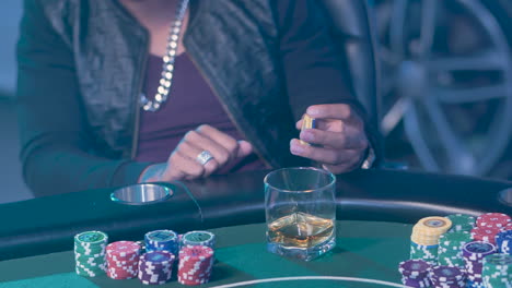 jugador de póquer sosteniendo fichas de casino con un vaso de whisky en la mesa