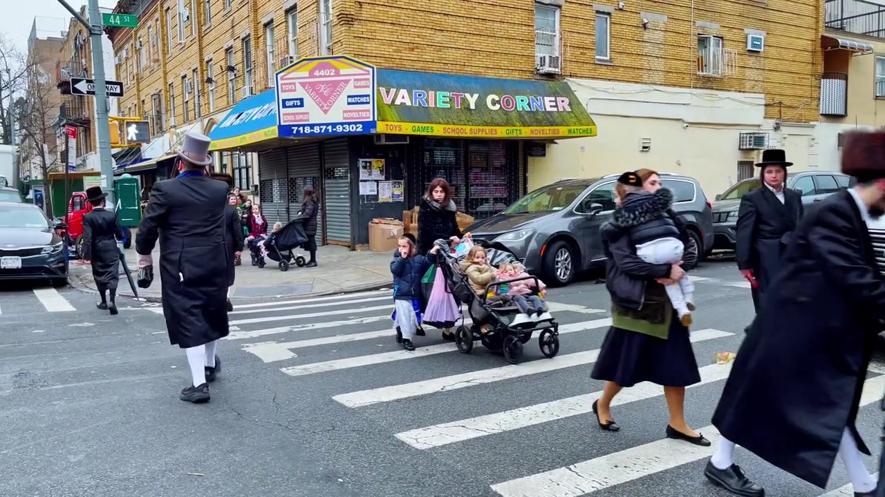 New York, USA, 9 March 2022: Orthodox Jewish pedestrians crossing Brooklyn street near stores. Pedestrians in Orthodox Jewish clothing cross 44 St by Variety Corner storefront, overcast daylight.
