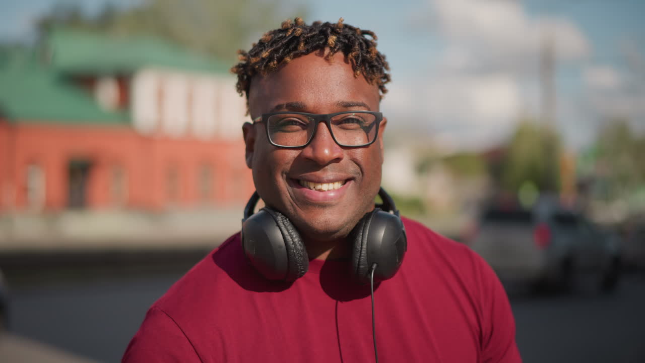 pessoa com fones de ouvido em esquina movimentada, planos médios capturam retrato sorridente contra prédio de tijolos vermelhos e telhado verde; as molduras transmitem um humor animado com DJ cumprimentando vizinhos, produtor procurando samples