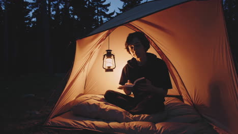person reading a book inside a tent at night