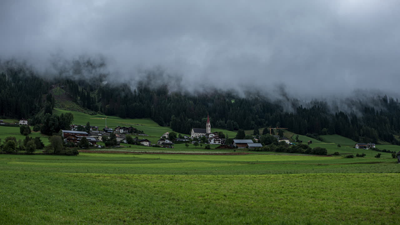 Tåge strømmer over typisk landsby i Dolomitterne med kirketårn, time-lapse