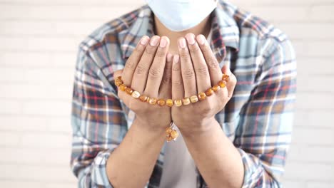 person praying with a mask on and rosary