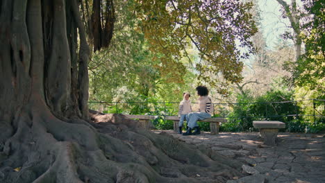 unrecognizable mother daughter sitting on park bench looking on beautiful tree.