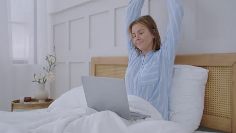 young millennial girl sitting on a bed in the morning uses laptop computer. caucasian woman home urban working online laptop bedroom bed