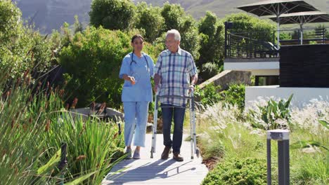 video of happy biracial female doctor taking care of caucasian senior man in rest home garden