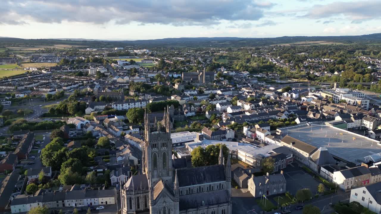 Vista aérea de drone em ângulo alto de Ennis, no Condado de Clare, mostrando a torre da catedral, ruas estreitas, casas e a paisagem circundante sob luz diurna suave e céu nublado.