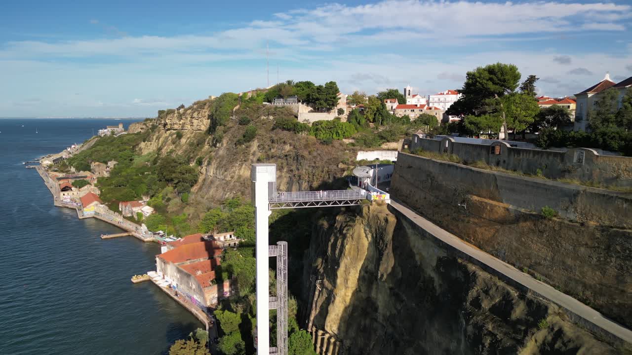 Breathtaking aerial footage captures a cliffside elevator in Nazaré, Portugal, linking a picturesque waterfront village to hilltop homes and a charming church tower, bathed in daylight