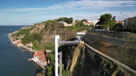 Breathtaking aerial footage captures a cliffside elevator in Nazaré, Portugal, linking a picturesque waterfront village to hilltop homes and a charming church tower, bathed in daylight