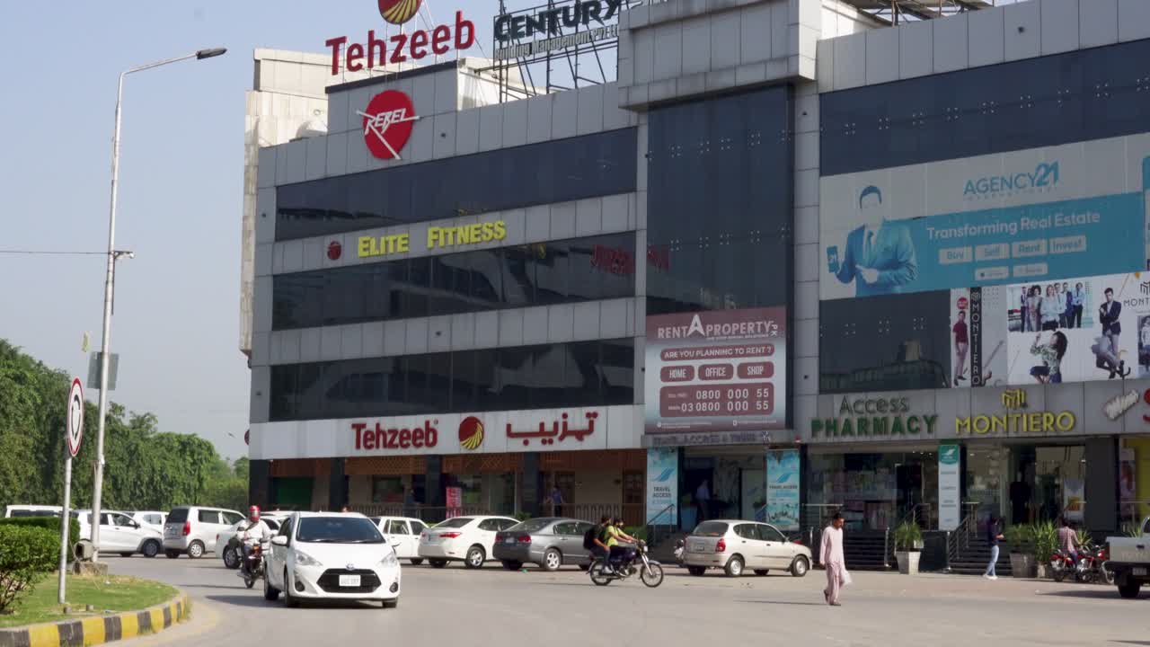 A shot capturing an impressive commercial structure situated along the main road, surrounded by cars under a clear blue sky.