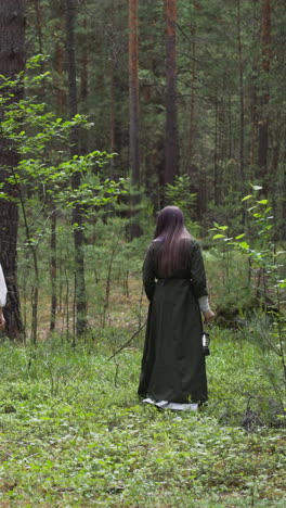 mysterious women wearing middle age dresses with lanterns walk through forest backside view. reconstruction of nature spirits worshiping ancient ritual