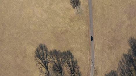 an aerial, top down view over a car driving through an empty park on a sunny day