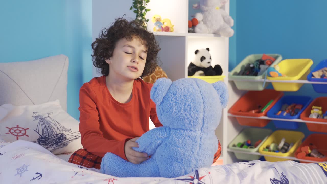 un lindo chico en pijama juega con su oso de peluche en su cama.