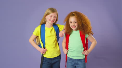 fotografía de estudio de dos niñas con mochilas yendo a la escuela sobre un fondo púrpura
