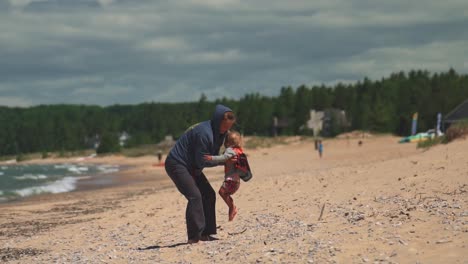 mother picks up toddler at sandy beach in slow motion