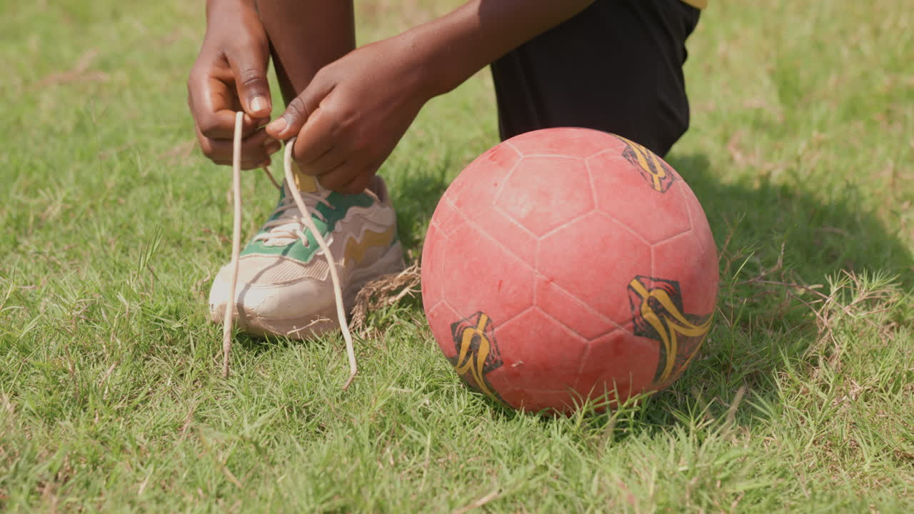 Menina amarrando atentamente os cadarços de sua chuteira. Adolescente ajustando seus tênis esportivos cuidadosamente antes do jogo. Jovem garoto amarrando meticulosamente suas chuteiras enquanto está ao lado da bola no quintal.