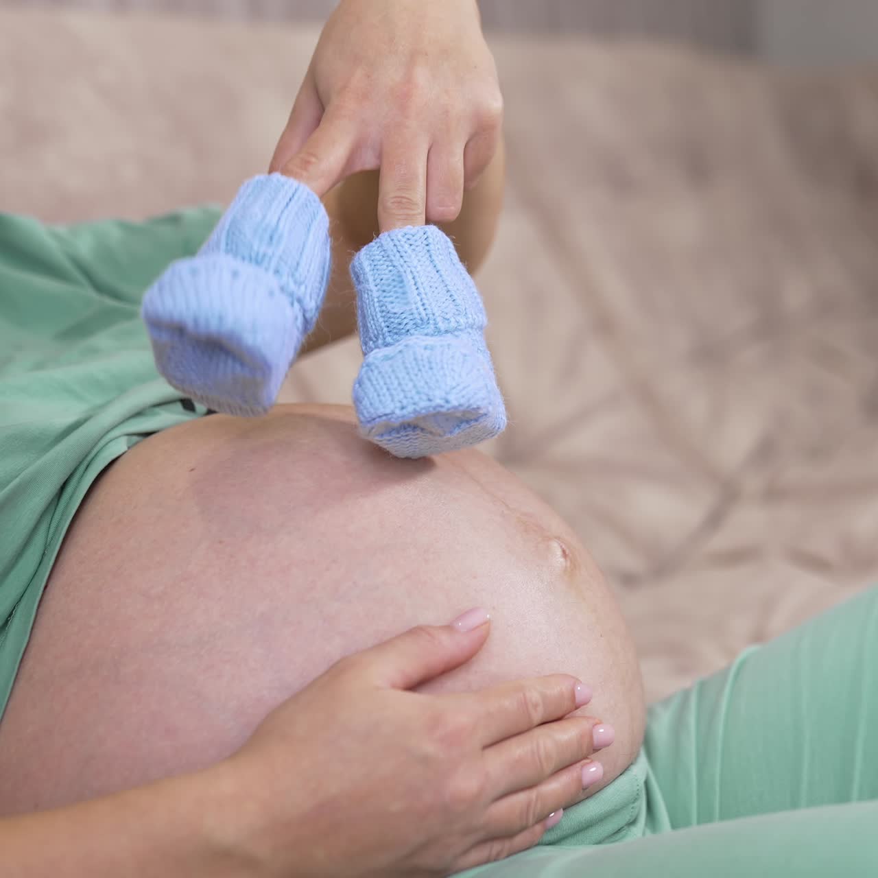 Pregnant woman holding knitted socks on a bare belly. Beautiful warm blue shoes for a future baby in woman's hands. Expecting a child