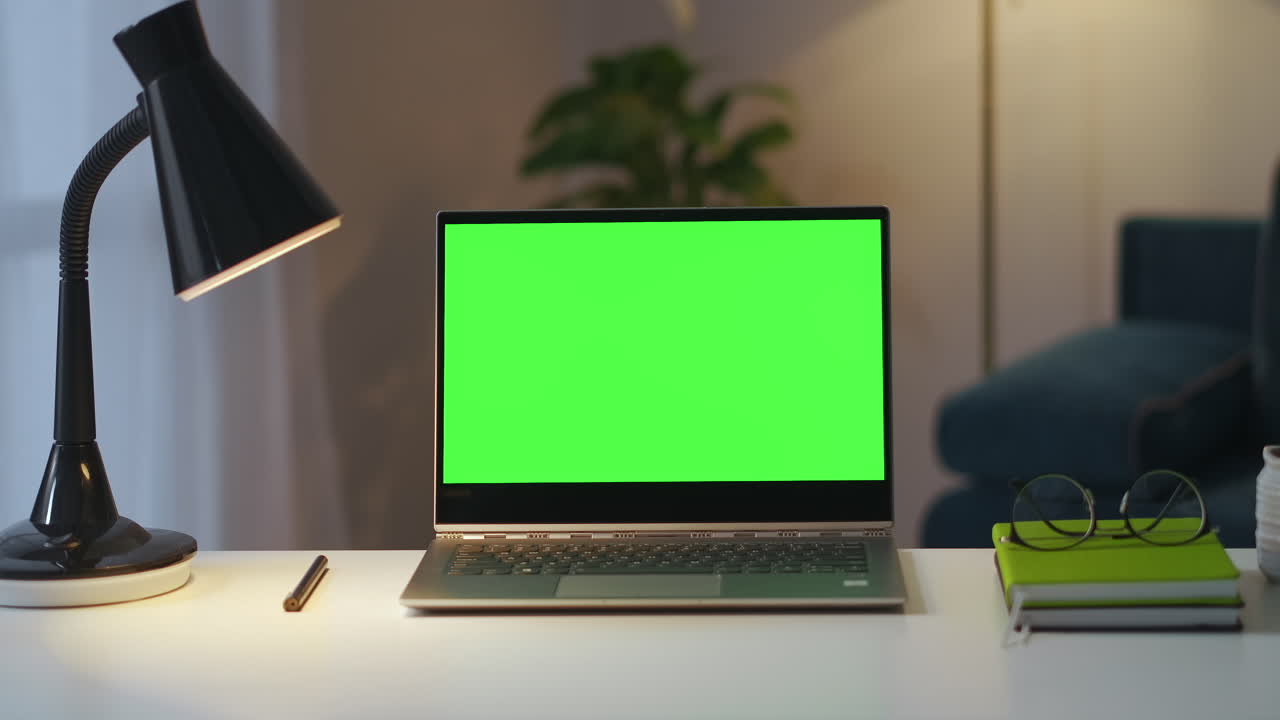 posto di lavoro di scrittore o freelancer in appartamento portatile con schermo verde per libri chiave chroma e lampada su tavolo colpo statico in ufficio a casa