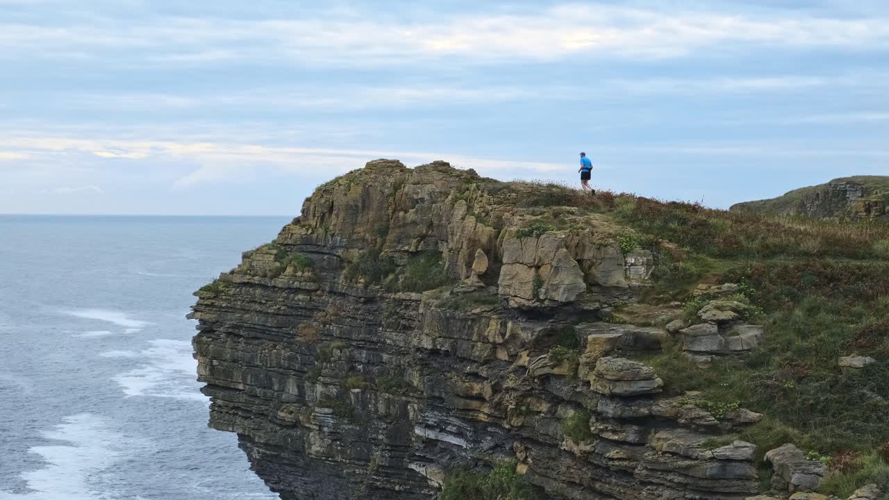 un joven caminando al borde del acantilado de la isla en isla junto con el mar cantábrico durante la puesta de sol