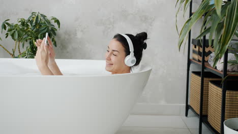 woman relaxing in bathtub with headphones and smartphone