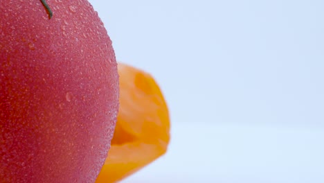 macro shooting of part of whole big red tomato and half part of yellow tomato with water drops. slowly rotating on the turntable. isolated on the white background. left half of the frame. close-up