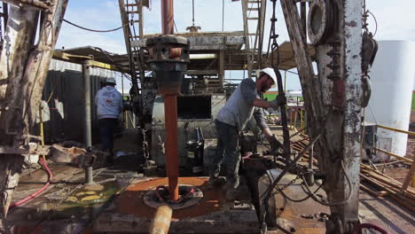 two men maintaining the equipment at oil drilling site. boring pole starts to rotate extracting resources.