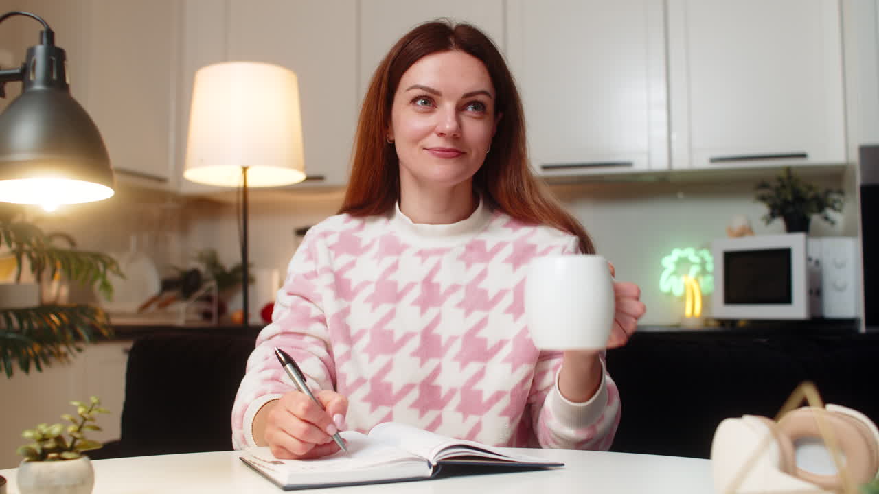 Donna adulta beve tè caldo di sera, si calma dopo una giornata intensa e scrive una lista di cose da fare in un quaderno, in tranquillità e concentrazione