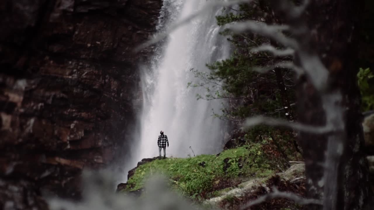Man standing in front of a huge waterfall, slow motion shot of a ...