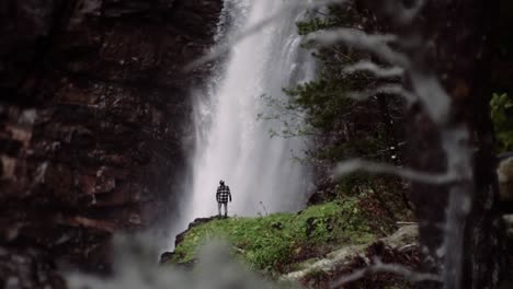 man standing in front of a huge waterfall, slow motion shot of a beautiful location during day time