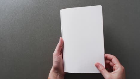 Close-up-of-hand-leafing-through-book-with-copy-space-on-gray-background-in-slow-motion