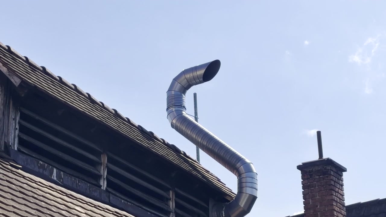An abstractly curved chimney on a roof and a straight chimney next to it, tilt up shot