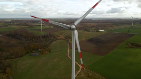 Aerial-shot-of-multiple-spinning-wind-turbines-for-renewable-electric-power-production-in-a-wide-rural-area-on-a-cloudy-day-in-4k