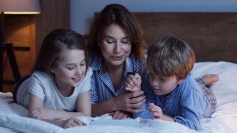 Kaukasische-Mutter-Und-Sein-Kleiner-Sohn-Und-Seine-Tochter-Liegen-Auf-Dem-Bett-Und-Beobachten-Etwas-Auf-Dem-Tablet