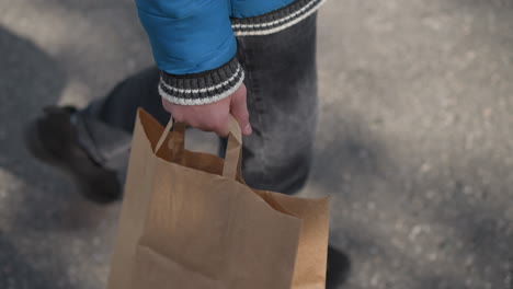 primer plano de piernas caminando en un área residencial, persona sosteniendo una bolsa de papel con sombras visibles en el suelo, con ropa casual, creando una escena urbana dinámica con iluminación suave