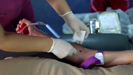 female hand with a tourniquet on the forearm. medic inserts a needle into the vein and a drop of blood appears. donor giving blood.