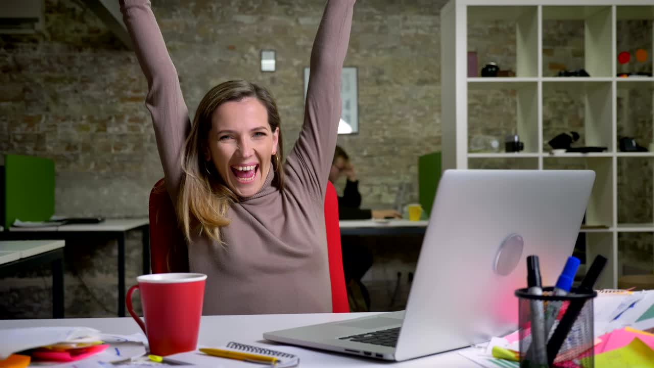 retrato en primer plano de una feliz empleada de oficina caucásica escribiendo en la computadora portátil y emocionándose por el éxito