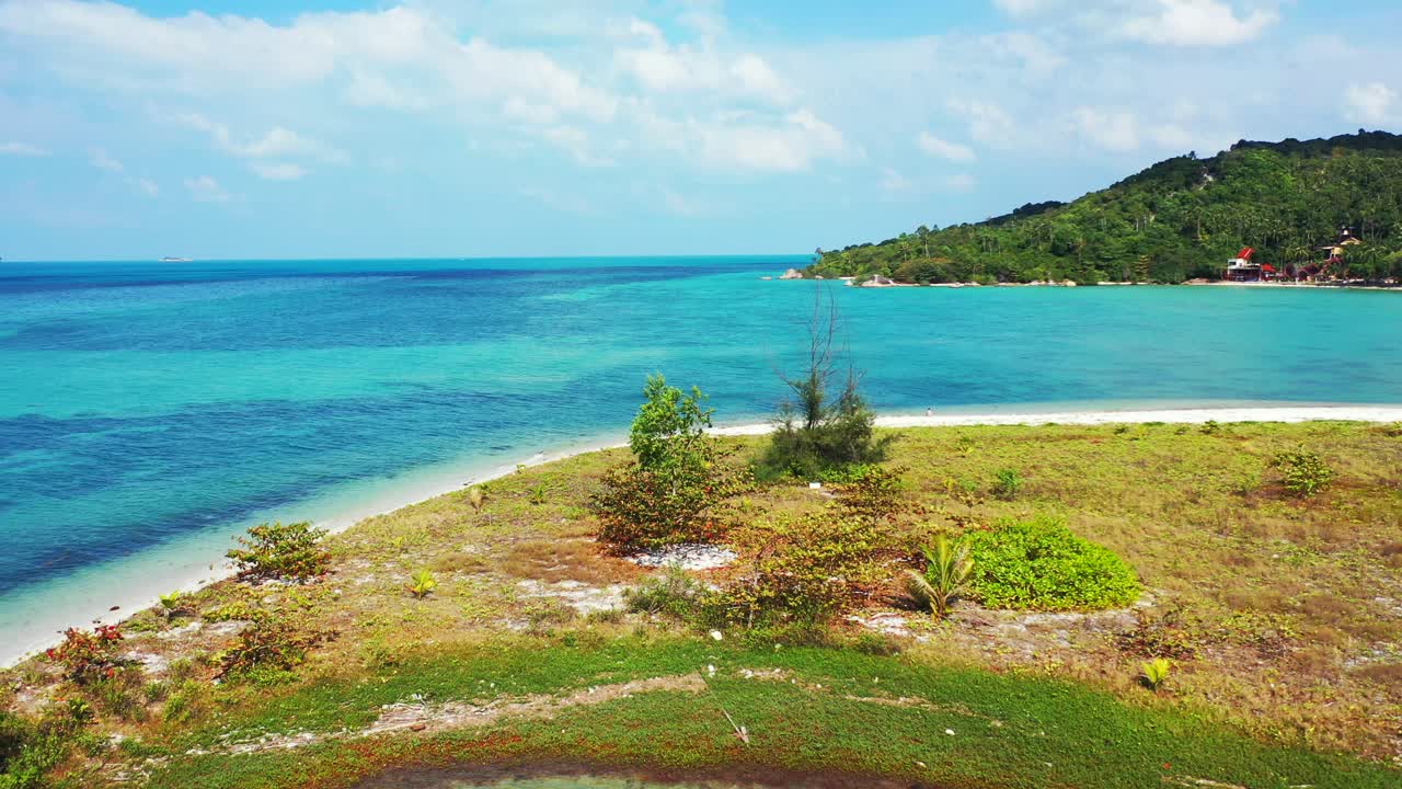 Beautiful shore of tropical coastline with grassland over tiny island washed by calm clear water of turquoise lagoon in Thailand