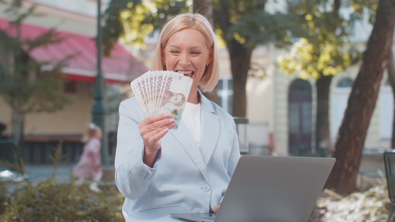행복한 성숙한 백인 사업가 ceo는 현금을 들고 도시 거리에서 노트북 컴퓨터를 사용합니다.