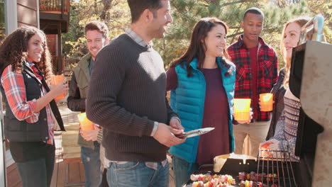 friends stand talking at a barbecue, one tends to the grill