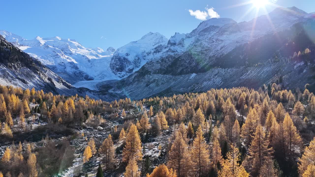 Alberi dorati autunnali incontrano le montagne alpine innevate sotto i bagliori del sole nella valle dell'Engadina, Svizzera