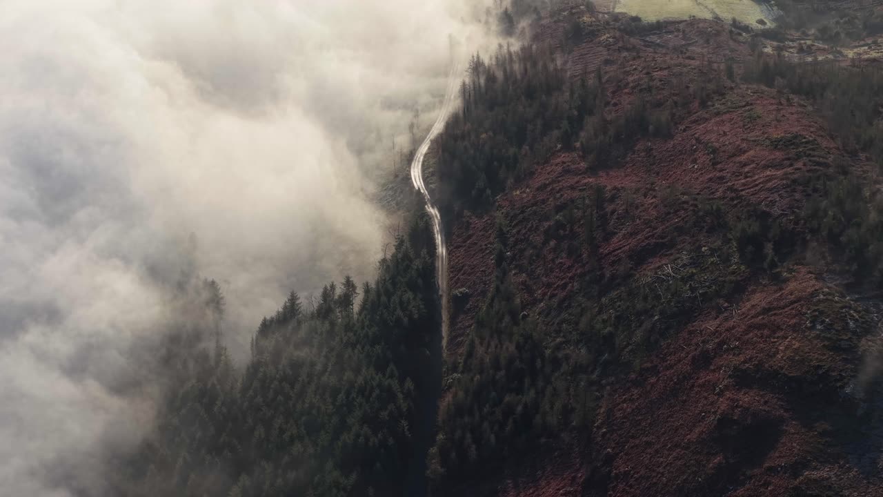 vista aérea de un paso de montaña a lo largo del bosque envuelto en niebla y nubes al amanecer en irlanda.
