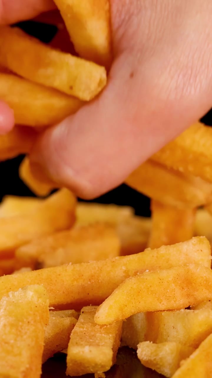 Human hand selects golden, crispy French fries under bright lighting, close-up, black background